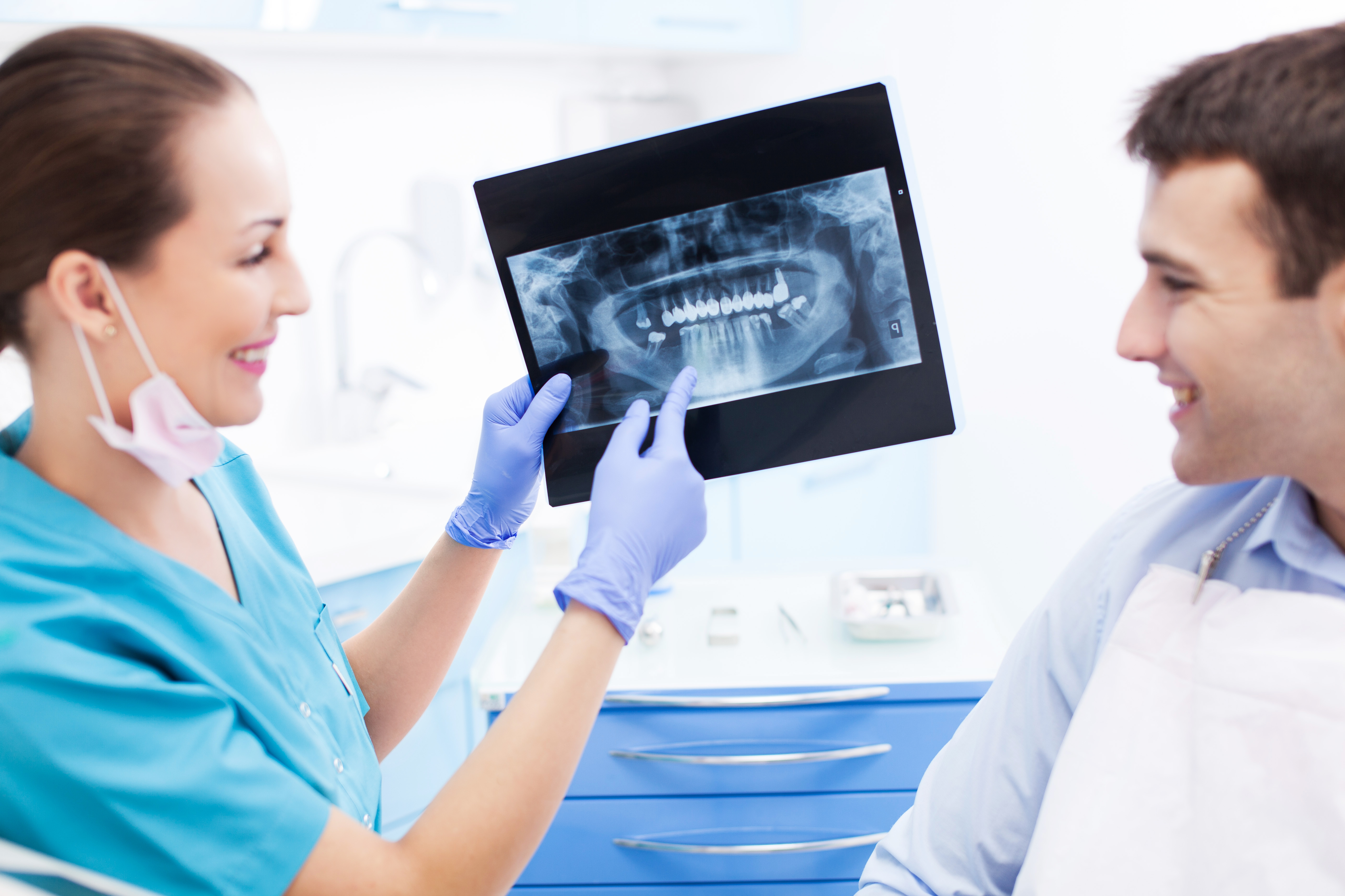 A dental professional holding a panoramic dental X-ray and discussing it with a seated patient